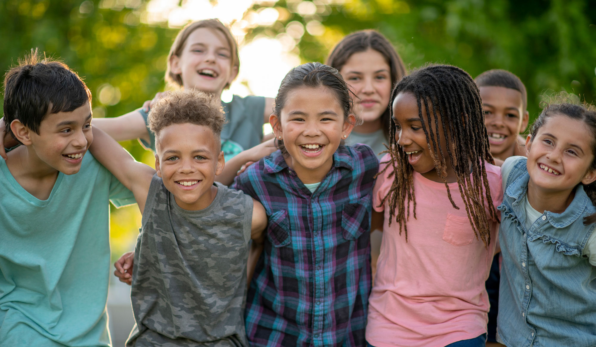 Group of school aged kids posing for photo with their arms around one another's shoulders