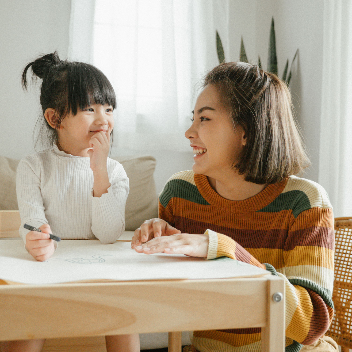 Mom and young daughter at a table drawing and smiling at each other