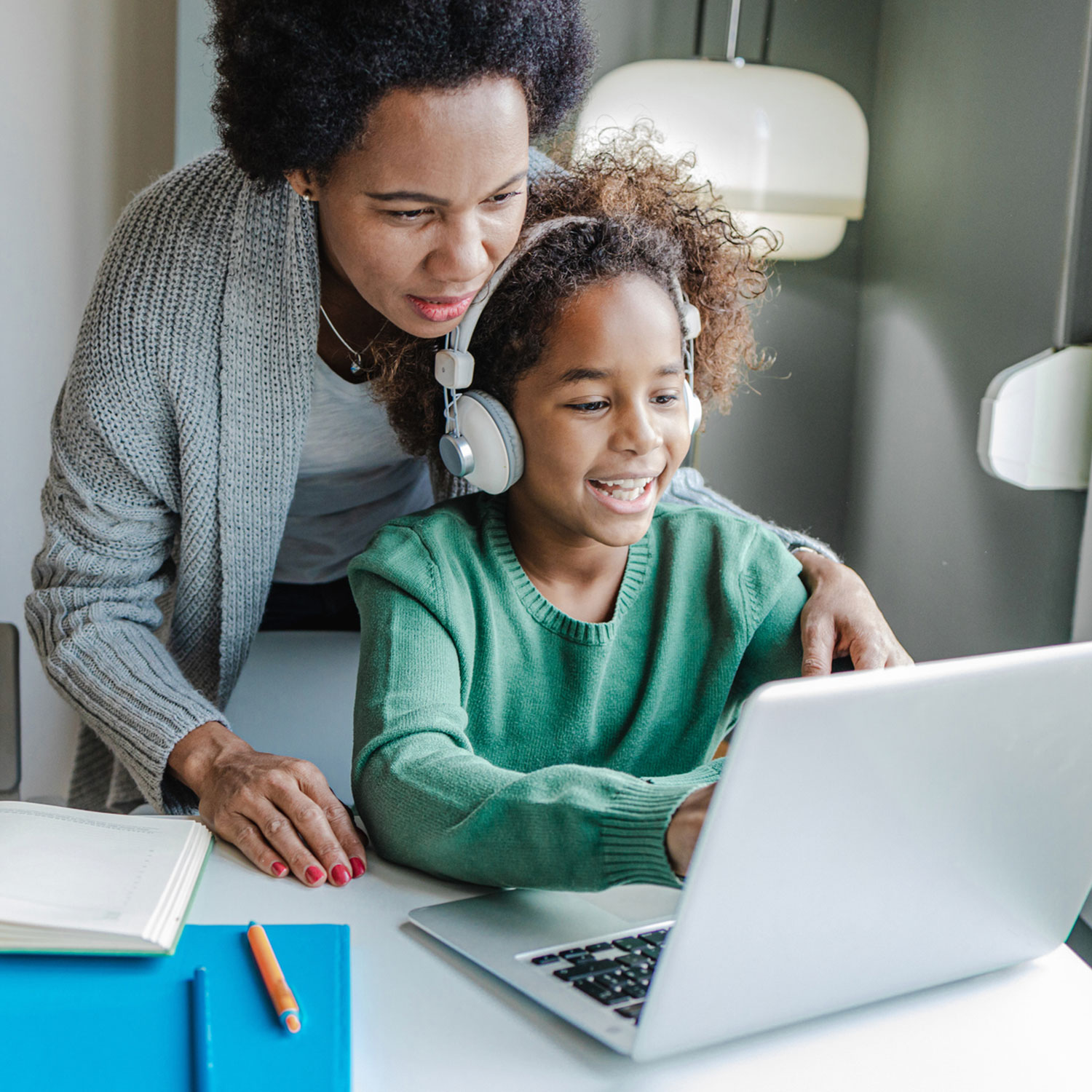 Woman looks over shoulder of young student working on a computer