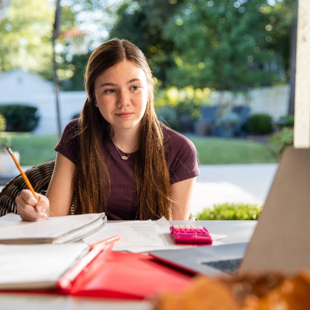 Student working at a table with a neighborhood background