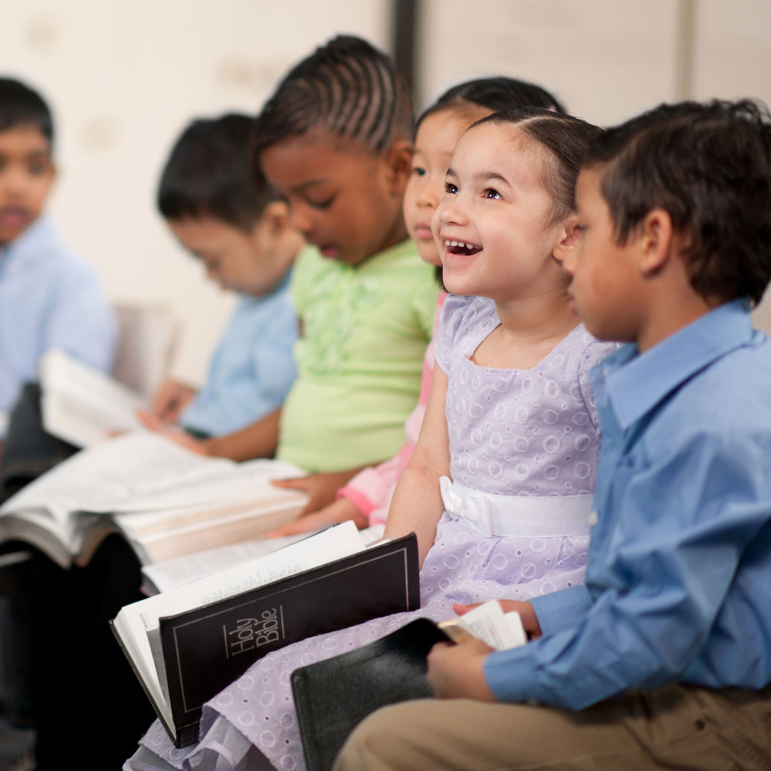 Young children sitting in a row holding Bibles