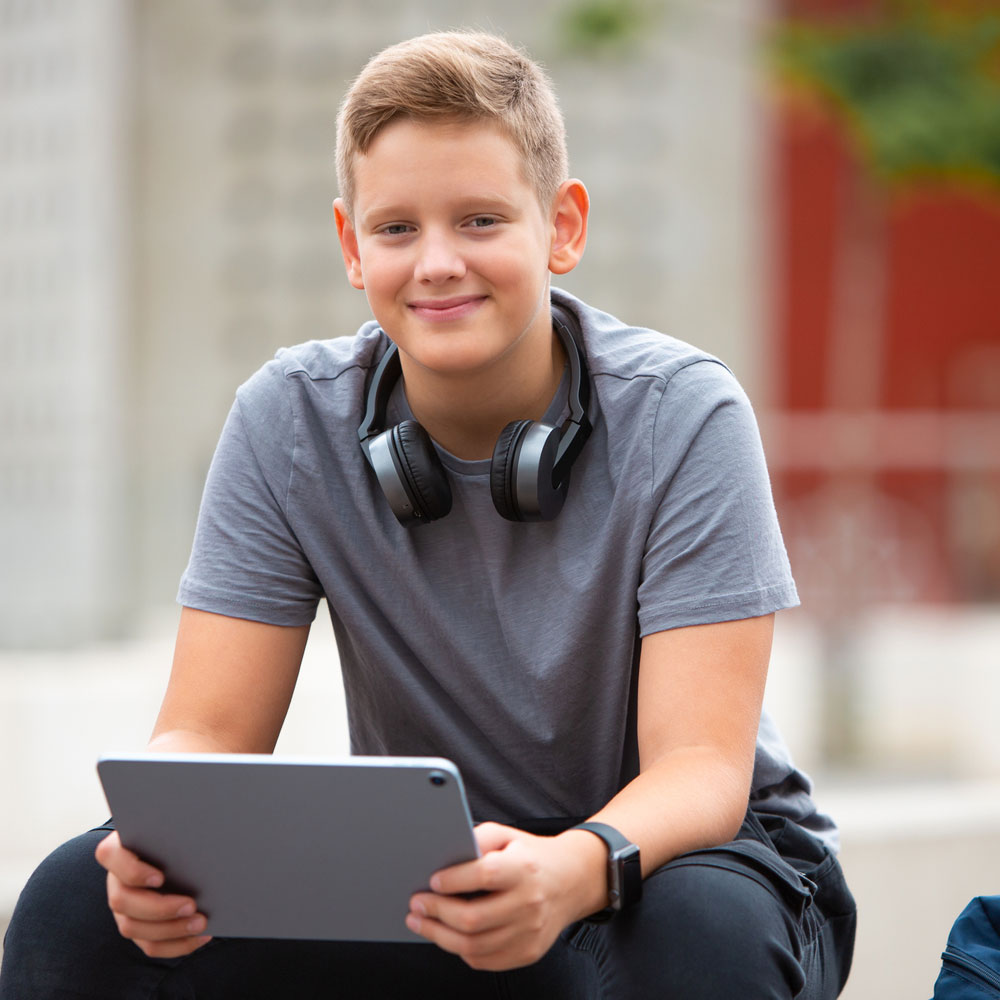 Student smiles while sitting with tablet computer.
