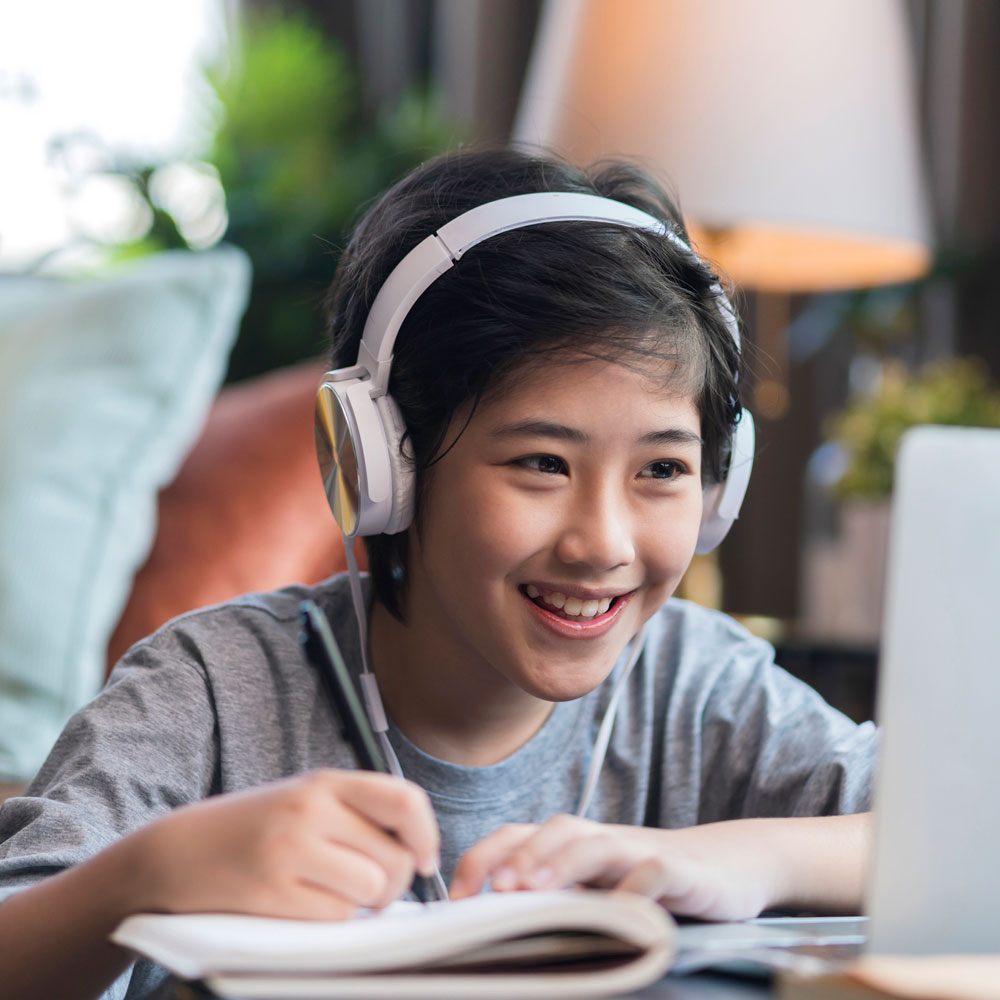 Student writes in a notebook while attending an online class.